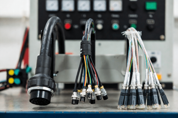 Three types of industrial cables laid out for comparison on a factory workbench: heavy power cable, multi-core control cable and shielded Ethernet cable, showing how electrical function determines conductor size, stranding and shielding needs in custom designs.