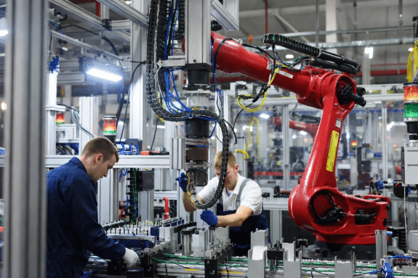 Realistic factory scene contrasting halted production line with technicians repairing failed drag chain cables on robot versus smooth running automation, illustrating total cost of ownership for custom cables