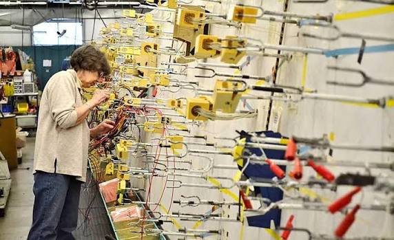 Technician inspecting and assembling electrical cables in an industrial manufacturing workspace, demonstrating cable testing, wiring organization, and quality control procedures for automation and electronic equipment production.