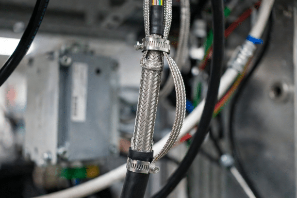 Close-up of correct 360° shield clamp termination on braided industrial cable with proper separation from power lines for EMI noise control