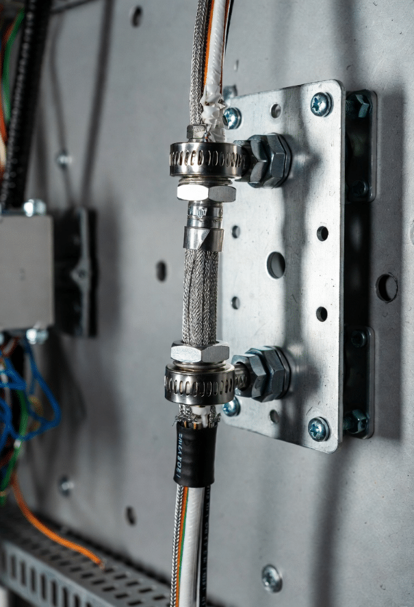 Close-up of properly terminated shielded servo cable with EMC gland and full-circumference grounding clamp on cabinet backplate
