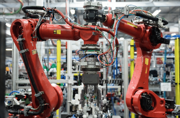 6-axis industrial robot arm performing dynamic motion with visible torsion cables routed along joints in a real factory setting, highlighting high-flex areas prone to failure modes