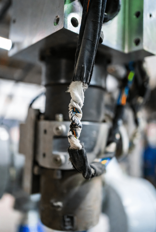 Comparison photo of damaged corkscrewed torsion cable versus properly routed cable in compact robot arm, illustrating common reliability issues in tight routing