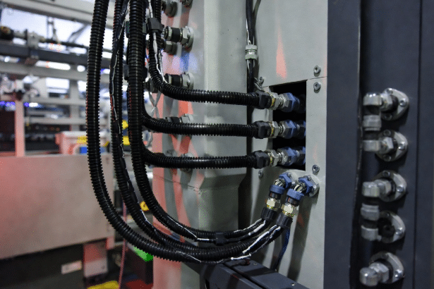 Industrial photo of custom drag chain cables entering machine frame and control cabinet via glands and connectors, showing real-world space and termination constraints in automation systems