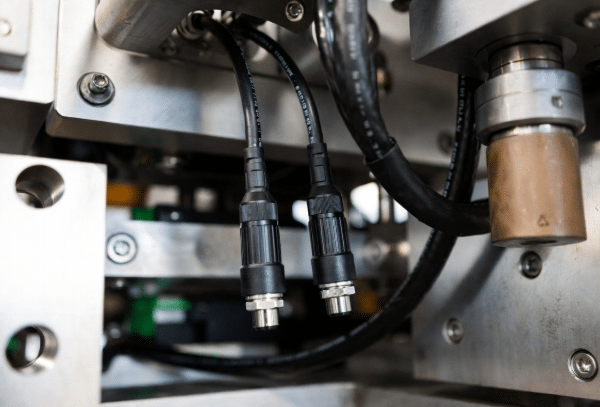 Close-up of black PUR-jacketed custom sensor cables with reinforced connectors operating in harsh industrial environment with oil exposure and mechanical movement for automation equipment