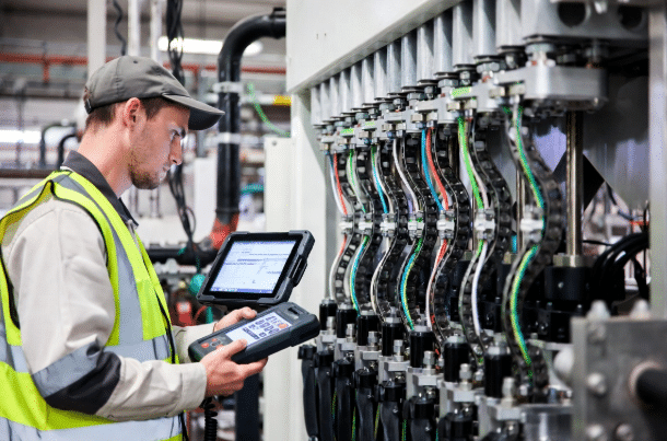 Technician performing condition monitoring and diagnostic checks on drag chain cables using digital tools in a modern manufacturing facility to support predictive maintenance