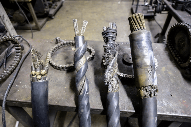 Composite view of several damaged high-flex drag chain cables exhibiting broken conductors, corkscrewing, jacket abrasion, and swelling, displayed for failure analysis in a manufacturing environment