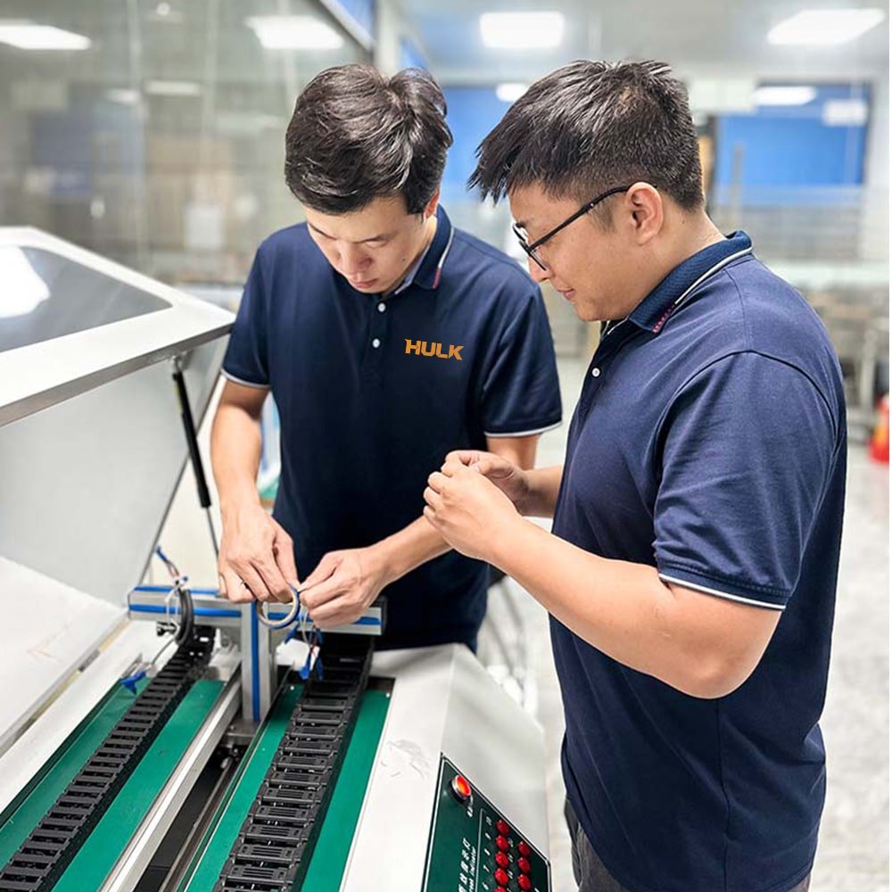 HULK factory technicians inspecting high-flex cable on automated production line with green conveyor and drag chain system, demonstrating precision manufacturing and quality control for industrial automation applications.