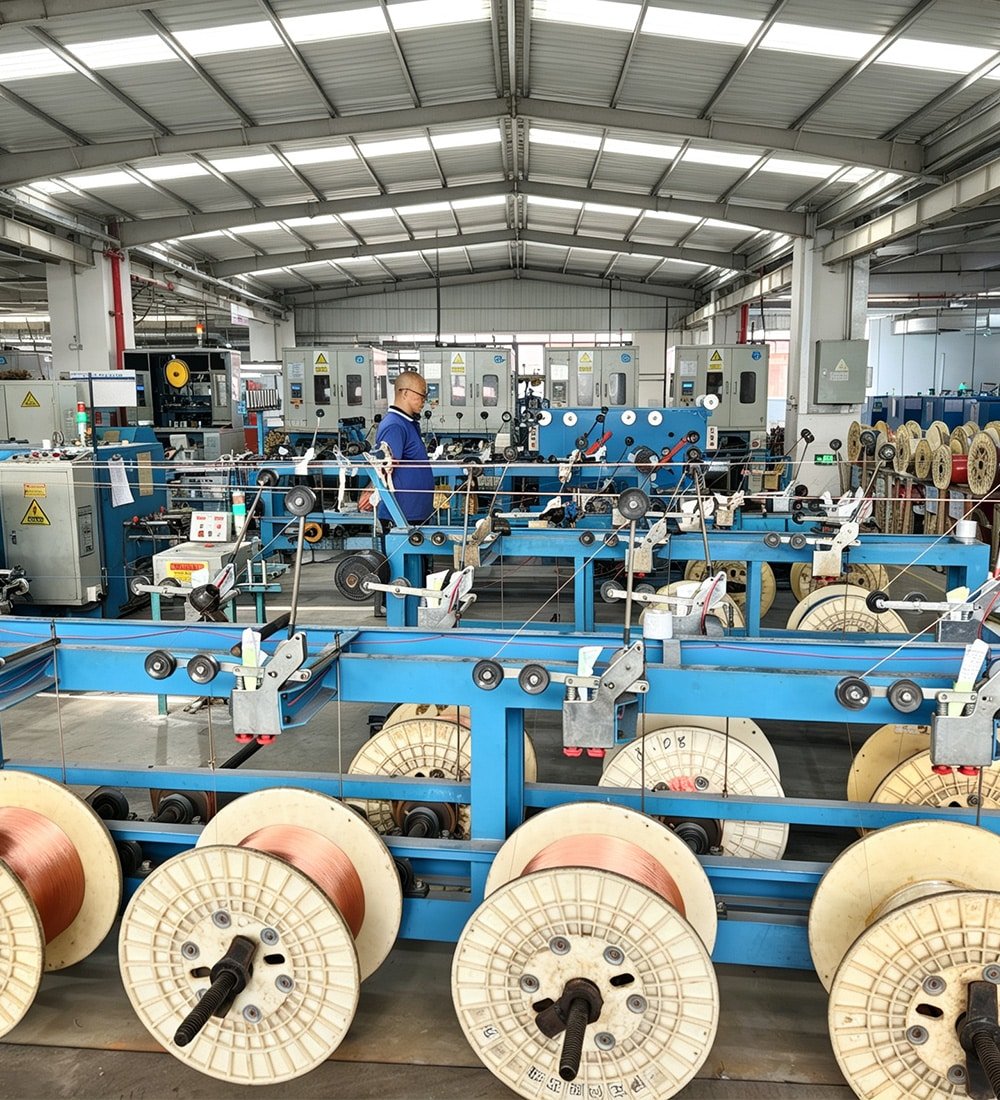 HULK factory floor showing the conductor stranding process with large copper wire reels feeding into blue high-speed machinery, supervised by a technician to ensure precision manufacturing of durable industrial cable cores.