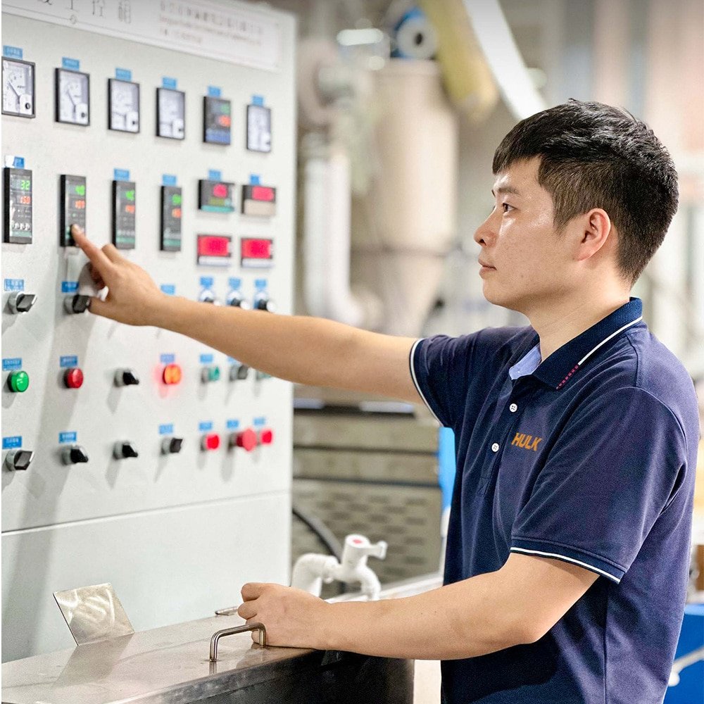 HULK engineer in branded uniform debugging an industrial electrical control panel, adjusting settings on the touchscreen interface, demonstrating professional on-site technical support and system integration expertise for automation projects.