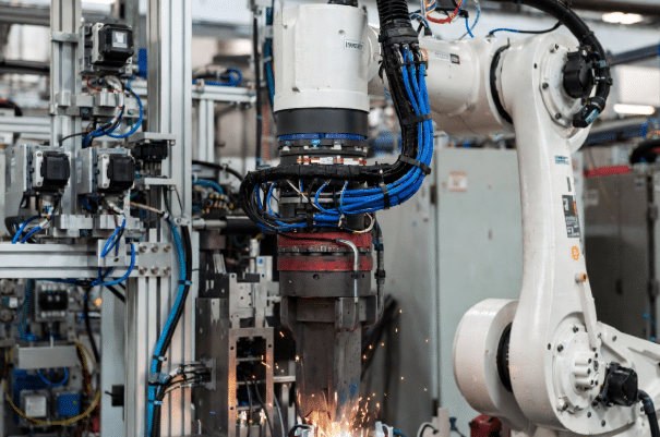 Six-axis industrial welding robot in high-EMI environment showing servo and encoder cables under torsion with sparks and drives nearby, illustrating need for shielded torsion cables for signal integrity in robotics