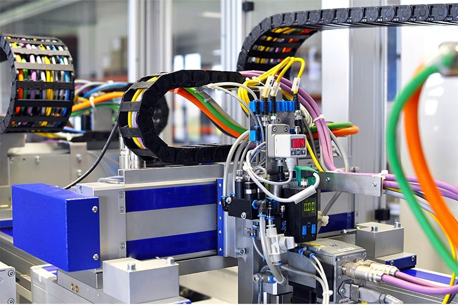 Multi-colored flexible cables moving smoothly inside a black drag chain on an automated assembly line, proving high-cycle durability for continuous motion applications