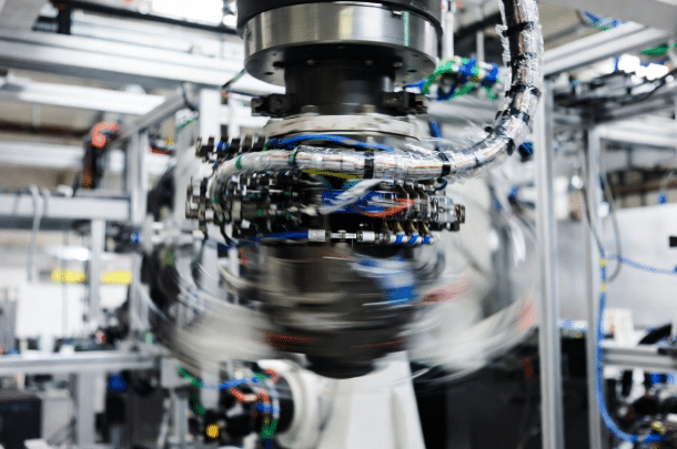 Close-up of 6-axis industrial robot wrist joint showing high-flex torsion-rated cables under dynamic twisting stress in automated manufacturing cell, illustrating impact of torsion angle on cable performance