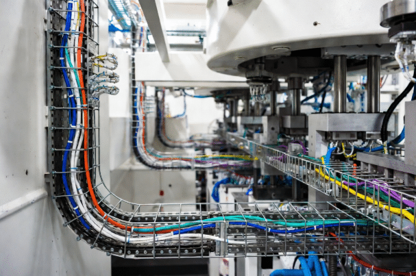 Realistic factory image of custom industrial cables properly installed through drag chains, conduits, and cable trays in an automation machine, highlighting correct motion and environmental considerations