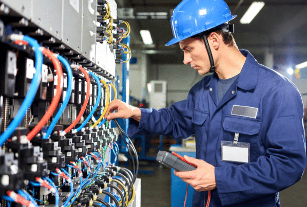 Industrial technician using tools to inspect and test sensor cables and connections on machinery, demonstrating proactive diagnostics for preventing automation downtime