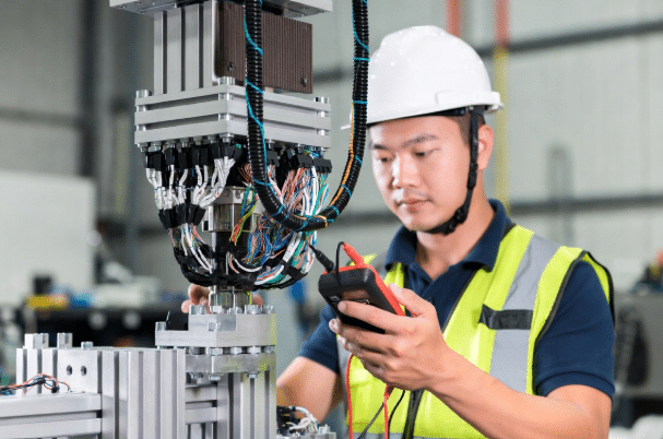 Factory technician conducting visual and multimeter inspection on industrial robot torsion cables for early failure diagnosis