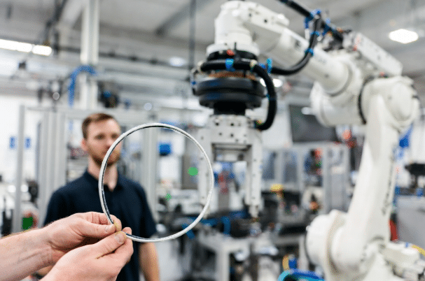 Technician holding a highly flexible limp robot torsion cable next to a 6-axis robotic arm in automation factory, illustrating flexibility vs long-term flex life demands