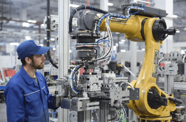 Engineer inspecting robot cable routing with service loops and clamps for combined bending and twisting motion in industrial robotics