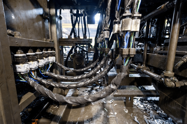 Close-up of robust servo cables with oil-resistant PUR jackets running through drag chains in a harsh manufacturing plant with visible coolant and metal debris, demonstrating durability for industrial automation