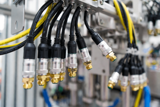 Close-up of rugged M12 connectors on shielded Industrial Ethernet CAT cables and sensor actuator cables installed on machinery, demonstrating proper shielding and routing for EMI protection in automation