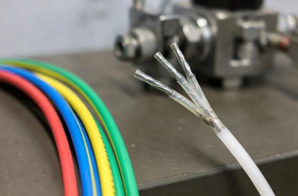 Professional comparison of colorful silicone insulated cables next to PTFE and PFA high-temperature wires with stripped ends on industrial workbench, highlighting material differences for engineering selection in hot environments