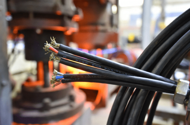 High-temperature silicone cables used as internal wiring in industrial floodlights and lighting fixtures near hot factory processes, realistic industrial photography