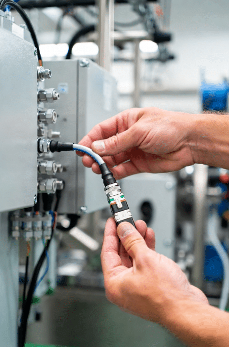 Close-up of technician installing high-flex modular sensor actuator cable with M12 connector into junction box on factory machinery, demonstrating fast and error-free wiring transition