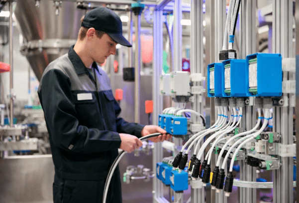 Skilled technician inspecting and routing high-flex sensor and actuator cables with distribution boxes and Industrial Ethernet connections in an industrial smart manufacturing environment