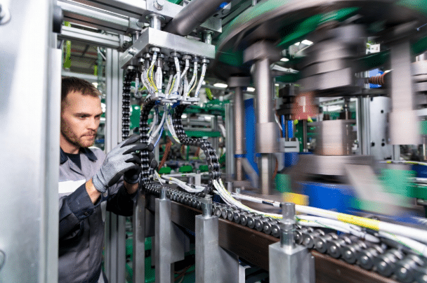 Maintenance technician inspecting drag chain system and flexible cables on automated production machinery, highlighting routine preventive maintenance strategies for drag chain cables in industrial setting