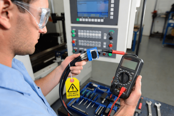 Industrial technician using multimeter for continuity and resistance testing on isolated servo cable during CNC troubleshooting procedure