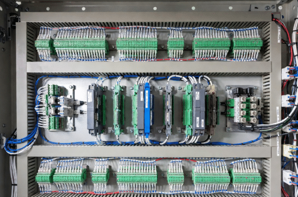 Professional view of neatly wired industrial control panel showing PLC IO modules, separated cable ducts, and properly routed sensor and actuator cables in a modern automation cabinet