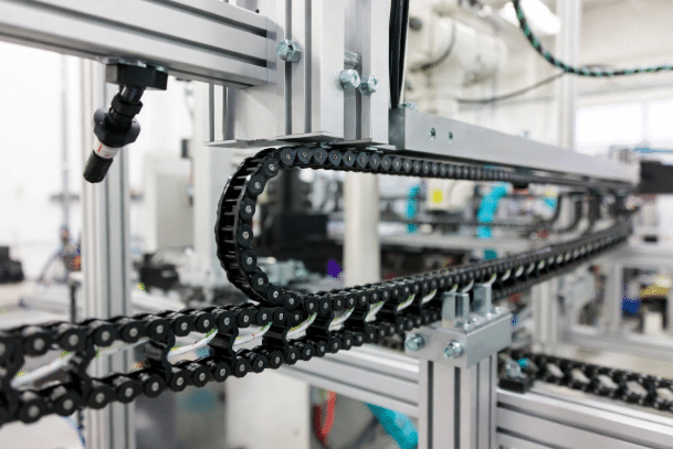 Professional view of a black energy drag chain carrying multiple Hulk high-flexible servo and robot cables with proper interior separators and optimal routing on automated machinery in a modern factory setting