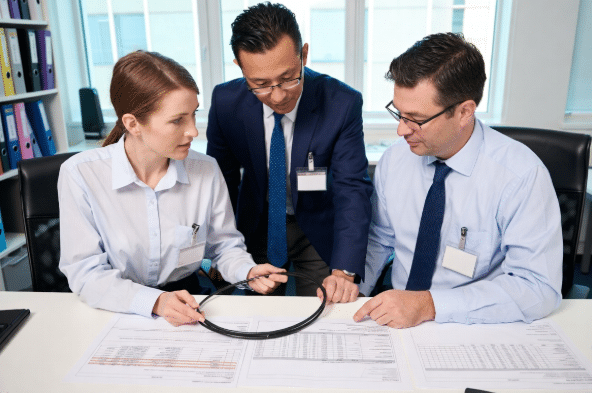 Two engineers in a modern engineering office examining a black LSZH industrial cable sample and technical drawings, collaborating on low smoke zero halogen cable specifications for OEM and system integrator projects