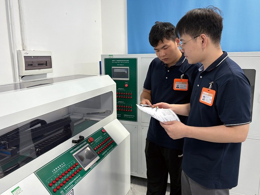 Two HULK engineers reviewing test data beside a TH8037 Drag Chain Cable Repeated Bending Tester, with multiple cable samples undergoing simultaneous flexing cycles; this scene demonstrates the brand’s commitment to batch consistency and human-verified quality control for high-cycle industrial applications.