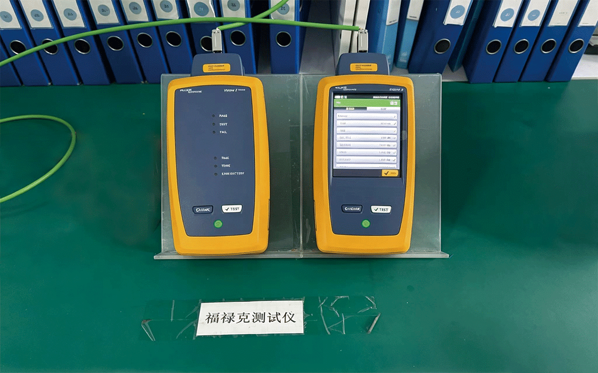 A Fluke Versiv cable certification tester setup with main and remote units connected by a green Ethernet cable; the display shows test results including PASS/FAIL status and detailed performance metrics, demonstrating HULK's commitment to validating every batch of network cables against international standards for bandwidth, crosstalk, and return loss.