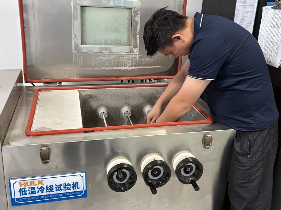 A HULK technician placing cable samples into a Low Temperature Cold Winding Test Machine chamber; this rigorous test verifies that the cable jacket and insulation remain flexible and crack-free at sub-zero temperatures, ensuring safe installation and operation in freezing environments like cold storage facilities or polar regions.