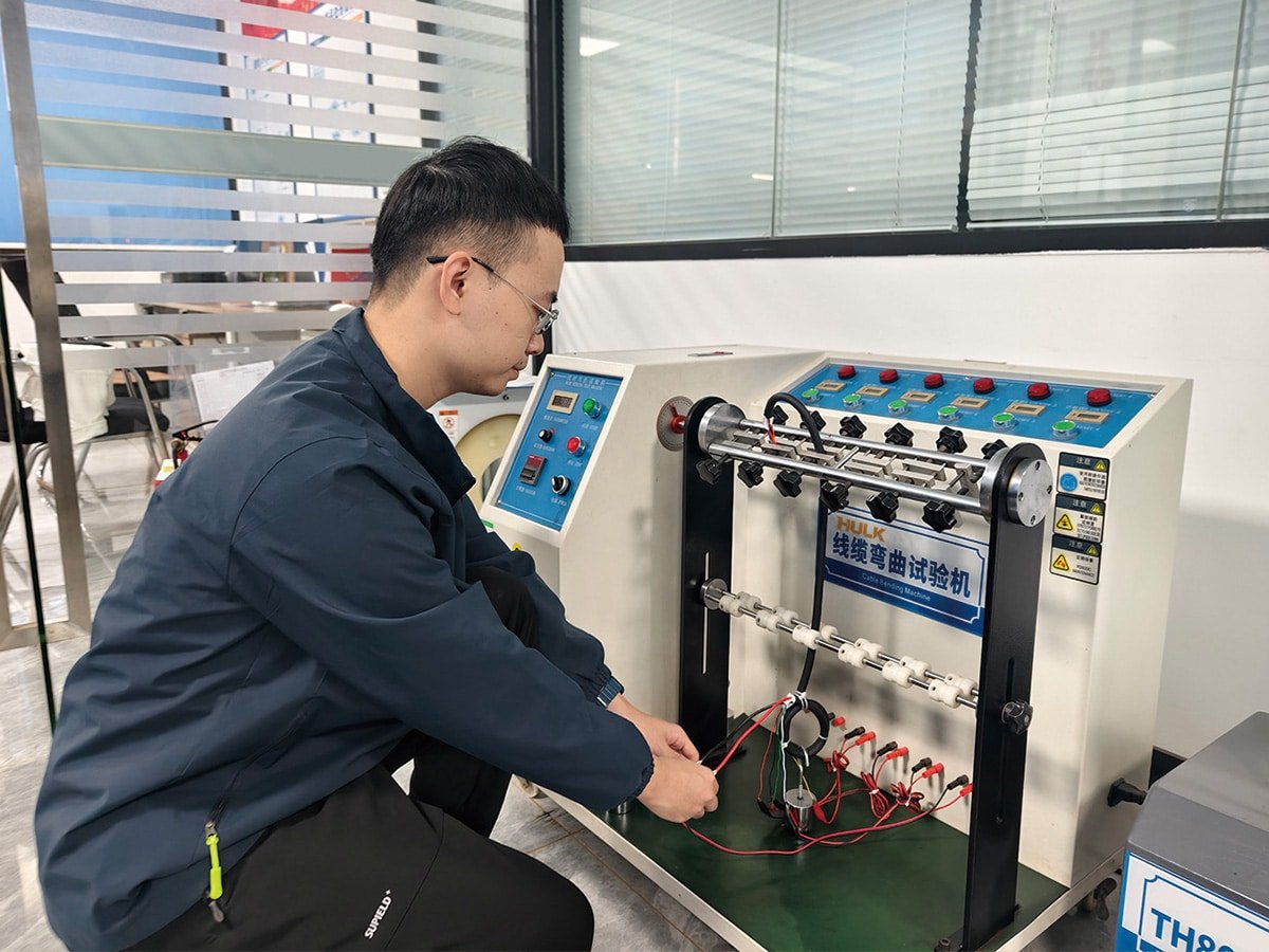 A HULK engineer connecting test leads to a multi-channel cable bending machine, with multiple samples undergoing simultaneous flexing cycles; this setup verifies both mechanical durability and electrical continuity under repeated bending stress, ensuring reliability in high-cycle industrial applications