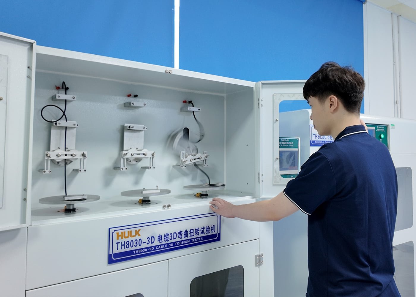 Engineer operating a HULK TH8030-3D Cable 3D Torsion Tester, subjecting black high-flex cables to rigorous repetitive bending and twisting cycles to validate mechanical durability and lifespan in a laboratory setting.