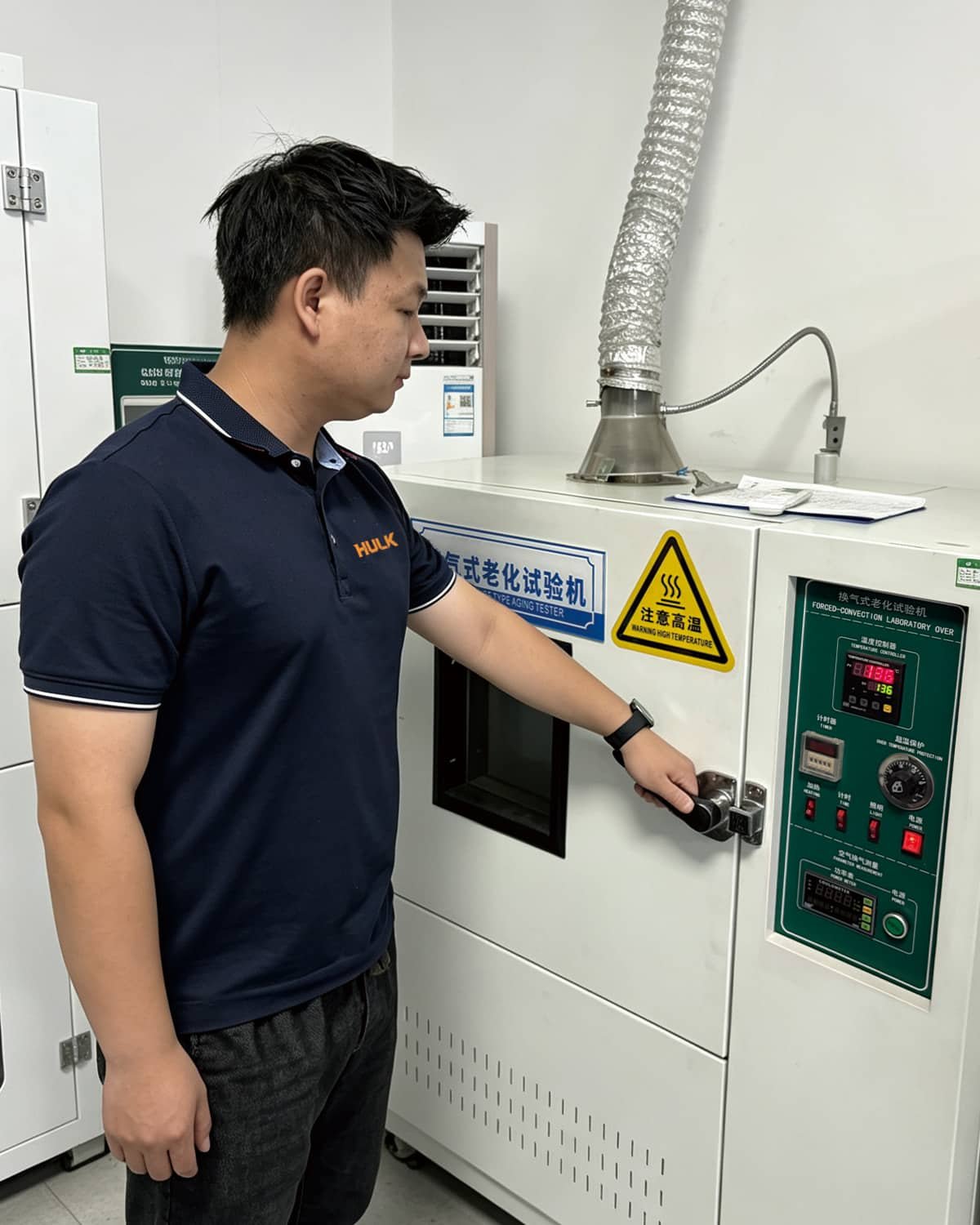 A HULK engineer operating a Forced-Convection Laboratory Oven (Thermal Aging Tester) to subject cable samples to prolonged high temperatures; this test simulates years of thermal exposure to evaluate insulation and jacket material degradation, ensuring long-term flexibility and electrical performance in hot environments like engine compartments or tropical installations.