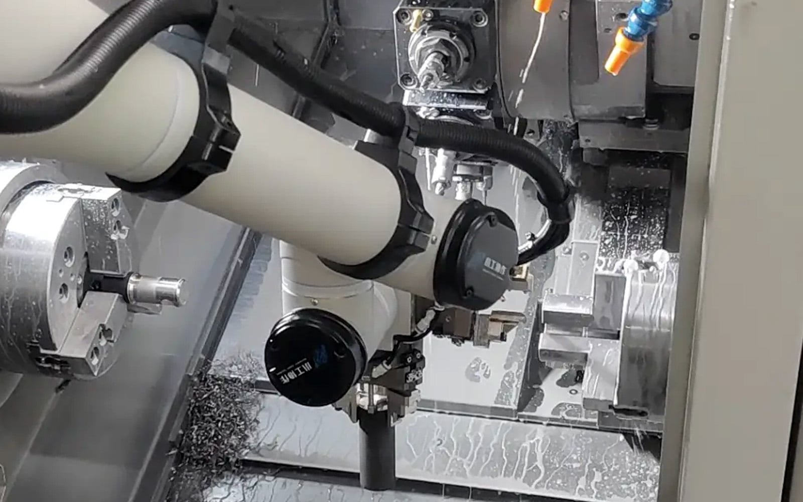 A white robotic arm operating inside a CNC machine tool chamber filled with metal chips and coolant, featuring HULK black high-flex cables routed along the arm; the scene demonstrates the cable's superior resistance to oil, coolants, and abrasive debris while maintaining reliable signal transmission under continuous heavy-duty motion.