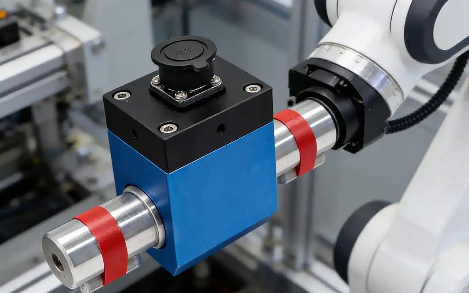 A close-up of a white collaborative robot arm with a blue and black end-effector tool; black HULK high-flex cables are routed through the compact joint, demonstrating their ability to maintain signal integrity and power delivery in tight spaces during high-speed, multi-axis operations for precision assembly tasks.