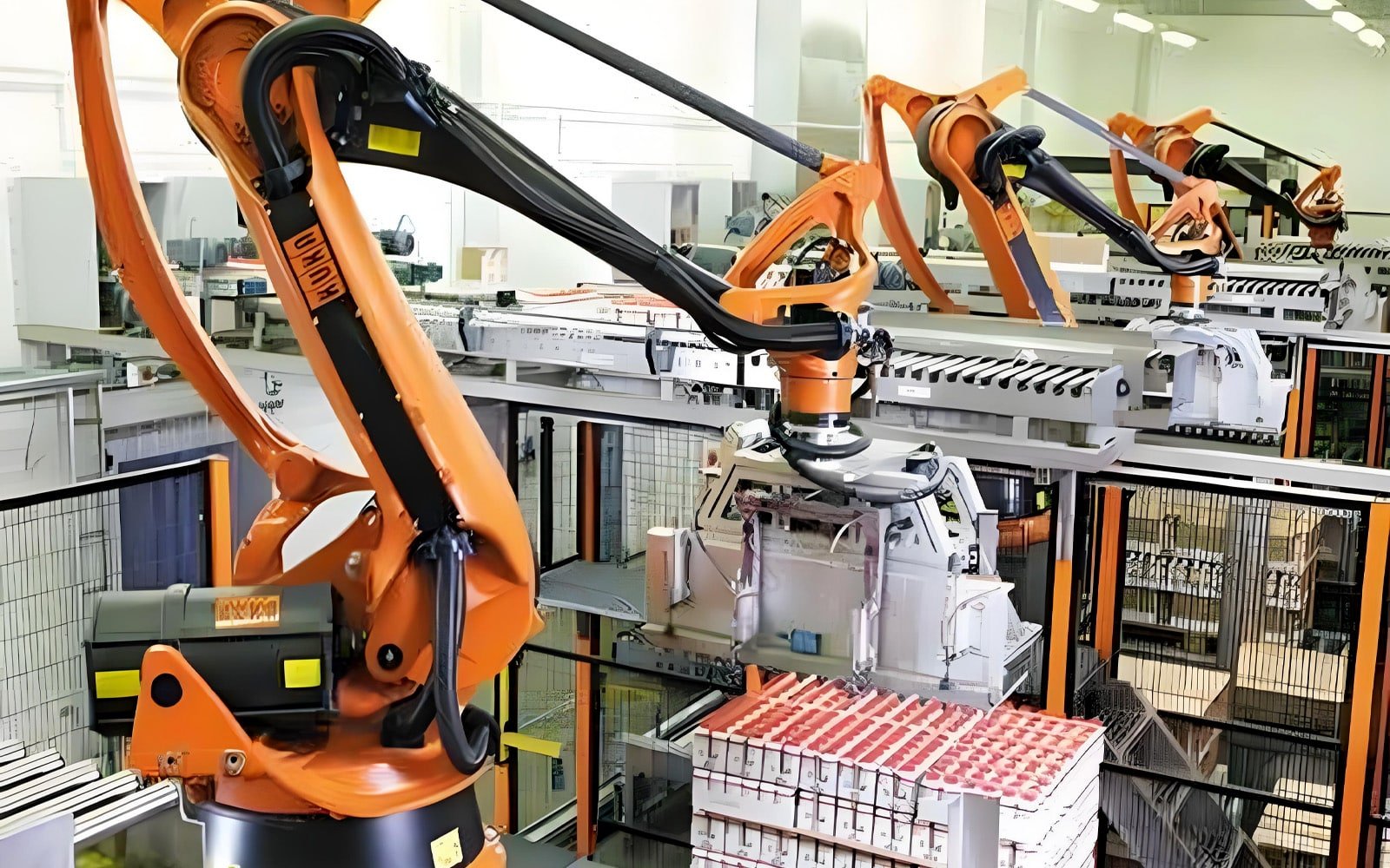 Multiple orange KUKA palletizing robots in synchronized operation, with black HULK high-flex cables routed along their articulated arms; the scene illustrates the cable’s ability to withstand continuous high-cycle motion and heavy payloads in 24/7 automated logistics environments, ensuring uninterrupted performance across multi-robot production lines.