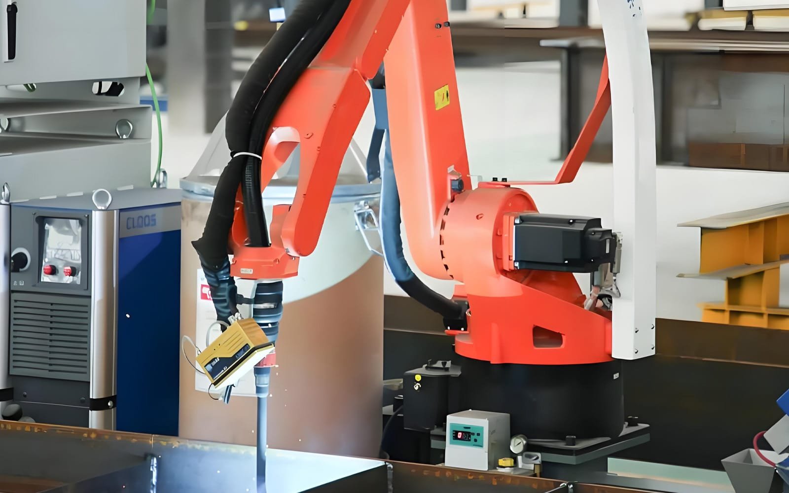 An orange welding robot arm in operation, with black HULK high-flex cables routed along its joints and moving dynamically during welding; the scene highlights the cable’s resistance to heat, sparks, and electromagnetic interference — essential for uninterrupted performance in automotive and heavy steel fabrication.