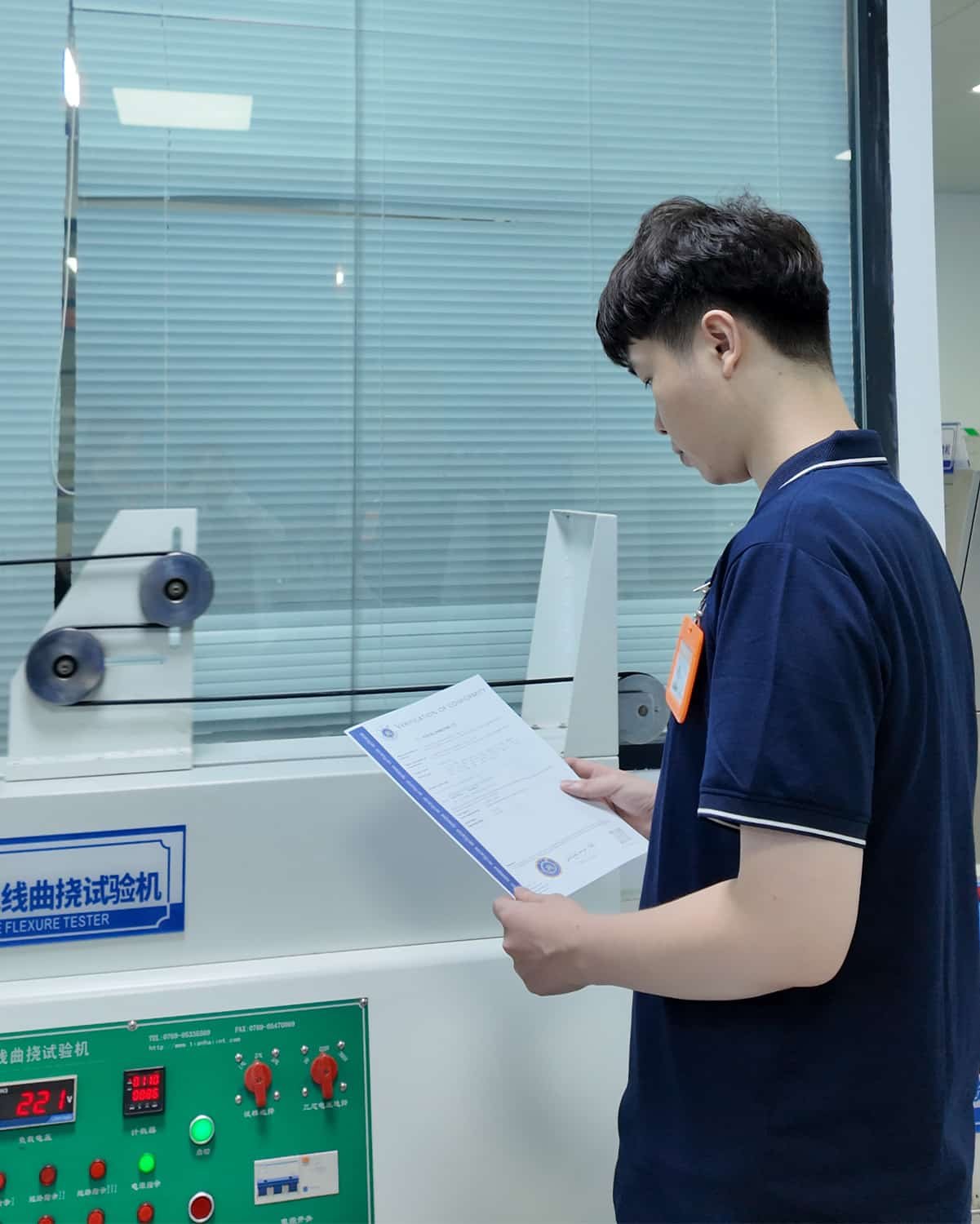HULK quality engineer reviewing a Verification of Conformity certificate in front of a cable flexure testing machine, ensuring test results meet international standards and compliance requirements.