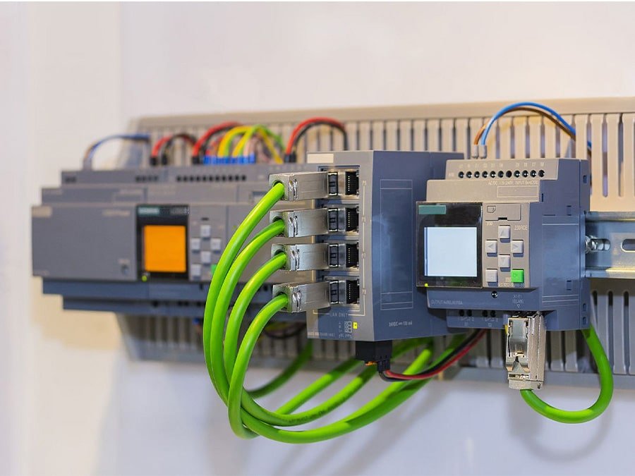 HULK industrial Ethernet switch connected via green cables to Siemens S7-1200 PLC module mounted on DIN rail; background shows multi-colored signal wires and control panel components — demonstrating seamless integration and reliable data communication in real-world automation systems.