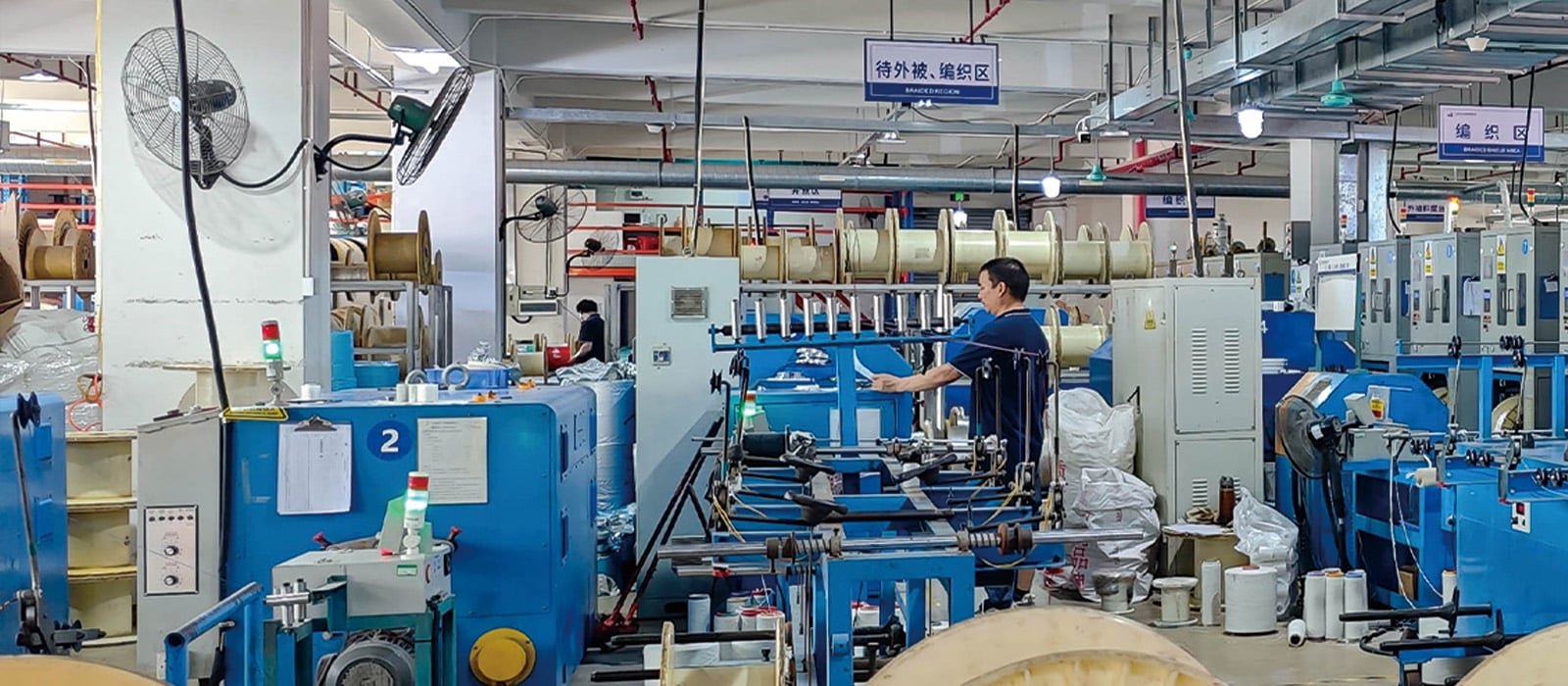 HULK manufacturing facility showing the designated Braiding & Sheathing Area with blue machinery and clear signage, where technicians operate high-speed braiding machines to apply shielding layers under strict process zoning.