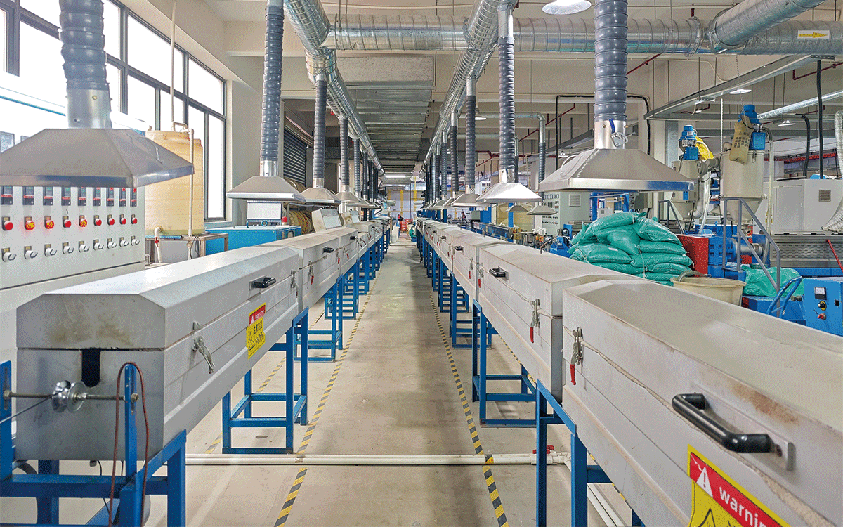 A perspective view of the HULK cable manufacturing workshop featuring parallel extrusion and cooling lines equipped with overhead silver ventilation ducts and exhaust hoods; yellow and black floor markings indicate safety zones, highlighting a controlled production environment designed for high-precision cable processing and efficient heat dissipation.