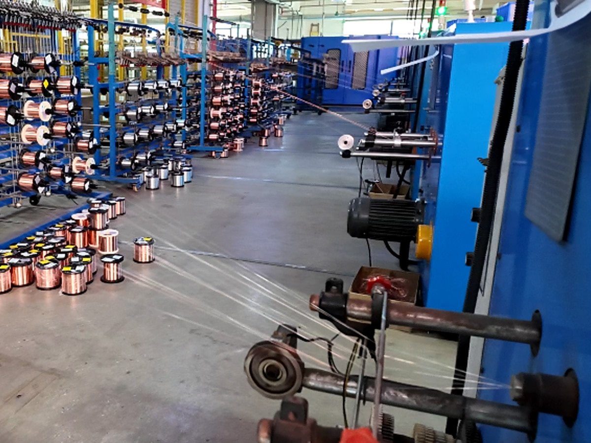 A wide-angle view of the HULK cable manufacturing facility, featuring rows of copper wire spools ready for processing and large-scale blue stranding machinery in operation; multiple fine copper strands are being drawn and twisted into cable cores, illustrating the company's advanced production capacity and strict quality control from raw materials to finished products.