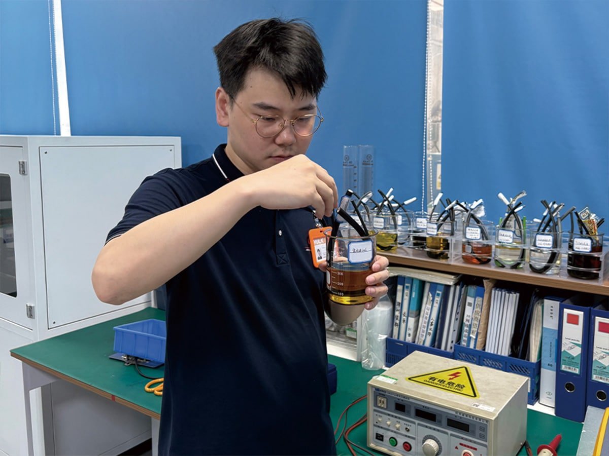 HULK lab technician conducting chemical resistance testing by immersing cable samples in beakers of oil and solvents, verifying material stability and durability against industrial fluids.
