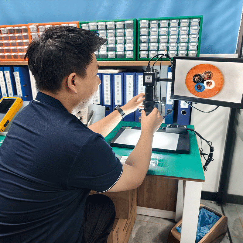 A HULK engineer using a digital industrial microscope to inspect the cross-sectional structure of a multi-core cable sample; the monitor displays a magnified view of the internal wire arrangement and insulation layers, demonstrating the company's commitment to verifying manufacturing precision, material consistency, and structural integrity at a microscopic level.